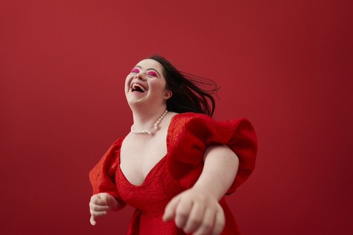 Happy young woman with with down syndrome laughing against red background. © Getty Images - Klaus Vedfelt