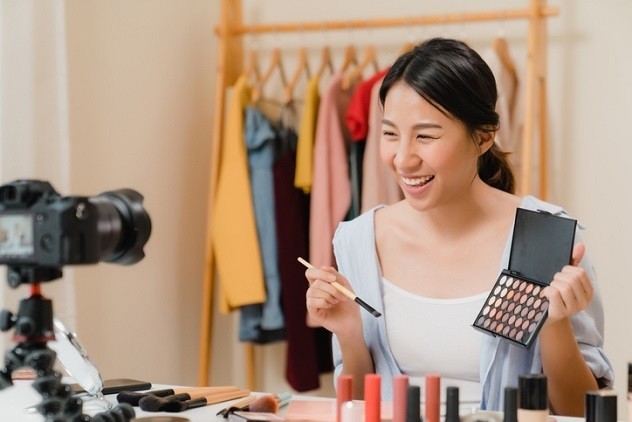 A beauty vlogger applies makeup in front of a camera - © Getty Images \ (Tirachard)